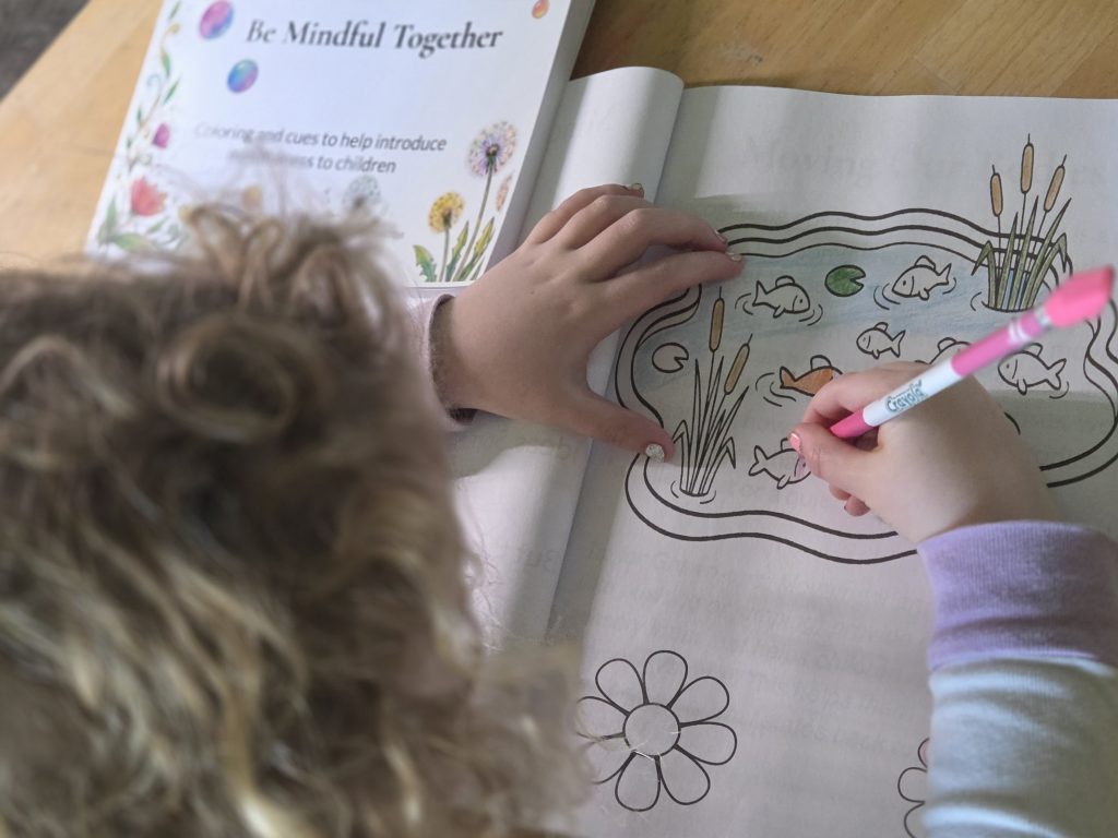 A child using colored pencils to draw in a mindfulness coloring book.