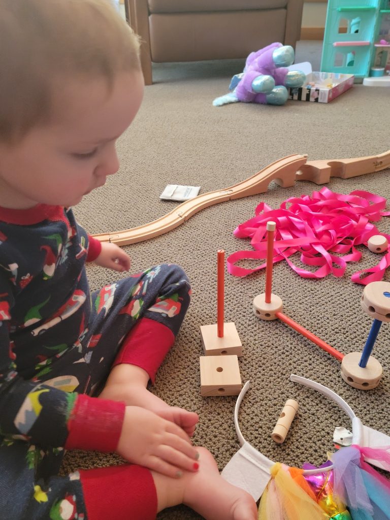 A child looking at trains and wooden building toys on a rug